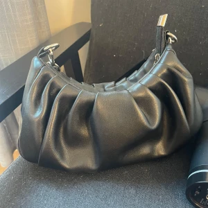 Svart axelväska med dragkedja - Snygg svart axelväska i syntetmaterial med dragkedja. Väskan har en stilren design med rynkade detaljer. Jag älskar den och den är super rymlig