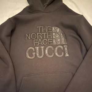Svart hoodie från Gucci x The North Face - Säljer en svart hoodie från samarbetet mellan Gucci och The North Face. Hoodien har en broderad logotyp på framsidan och en klassisk känguruficka. Perfekt för en stilren och bekväm look. Pris går att diskutera helt ny aldrig använt 