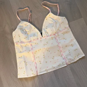 Blommigt sommar linne - Super gulligt linne som är helt nytt! Så gulligt och perfekt inför sommar och vår. Rosa blommor mot vit bakgrund och detaljer i rutigt rosa. Justerbara band, skriv om du har frågor 🩷🩷 (säljer då den ej passade mig!)