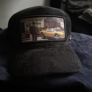 Svart keps från Maggiore - Snygg svart keps från Maggiore med en unik bilddetalj på framsidan. Kepsen har en justerbar rem baktill för perfekt passform. Perfekt för dig som vill ha en stilren och cool look.