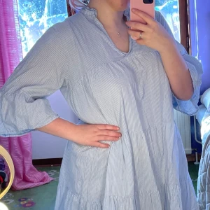 Blå och vit randig klänning - Säljer en luftig och bekväm blå och vit randig klänning med v-ringning och trekvartsärmar. Perfekt för en avslappnad stil. Klänningen har en lös passform och volangdetaljer som ger en fin rörelse. storlek L/XL! Luftig! Perfekt till sommaren! Använd några gånger 