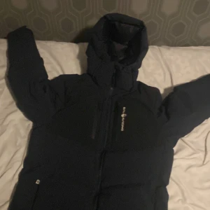 Mörkblå dunjacka från sailracing - Säljer en mörkblå dunjacka från Peak Performance. Jackan har en hög krage och en justerbar huva för extra skydd mot kyla. Den är utrustad med dragkedja och flera praktiska fickor. Perfekt för kalla vinterdagar.