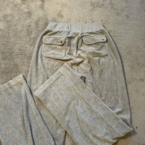 Grå mjukisbyxor från Juicy Couture - Snygga grå mjukisbyxor från Juicy Couture med elastisk midja och praktiska fickor både fram och bak. Perfekta för en avslappnad stil. Byxorna har en diskret logga på framsidan och är gjorda i ett mjukt material för extra komfort.💯🩶🤍💟