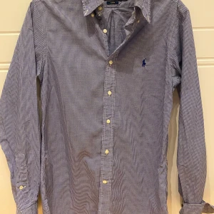 Blårutig skjorta från Ralph Lauren - Snygg blårutig skjorta från Ralph Lauren i slim fit. Skjortan har långa ärmar och klassiska knappar framtill. Perfekt för en stilren look.