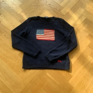 Mörkblå stickad tröja från Ralph Lauren - Säljer en snygg mörkblå stickad tröja från Ralph Lauren med en stor amerikansk flagga på bröstet. Tröjan har långa ärmar och RL-broderi i rött. Storlek S men ganska stor i storleken.