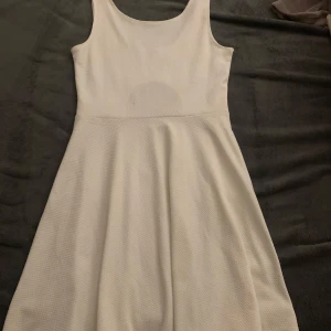 Vit ärmlös klänning - Säljer en stilren vit ärmlös klänning med rund halsringning och en snygg öppen ryggdetalj. Perfekt för sommarens varma dagar. Klänningen har en skön passform och är gjord i ett lätt material. Skulle absolut passa som student klänning!!