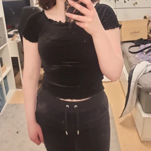 Svart ribbad topp från Kappahl - Säljer en svart ribbad topp från Kappahl med korta ärmar och en söt volangdetalj vid ärmslut och hals. Perfekt för en stilren look. Passar bra till både jeans och kjol. Defekter förekommer men inget som syns jättetydligt när den sitter på. Skulle säga att det är som en XS i storleken 🖤