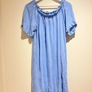 Ljusblå klänning med resårdetaljer - Säljer en ljusblå klänning med resårdetaljer vid halsringningen. Klänningen har korta ärmar och en avslappnad passform. Perfekt för en somrig look! 💙