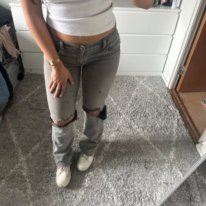 Grå jeans med slitna detaljer - Snygga grå jeans med slitna knän och en avslappnad passform. De har en låg midja och klassisk femficksdesign. Perfekta för en casual look med en t-shirt eller hoodie. Dessutom justerbar i midjan och ett väldigt stretchigt material