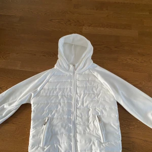 Vit cardigan jacka från verani clothing |storlek M - Säljer en stilren vit cardigan jacka med huva. Jackan har dragkedja framtill och två praktiska fickor med dragkedjor.  Inte använd en ändå gång!