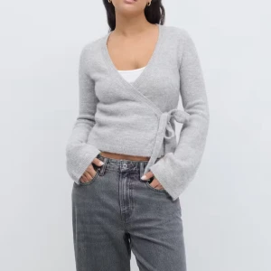 Grå omlottkofta med knytband - Säljer en super viral stilren grå omlottkofta från ginatricot💕💕💕 Koftan har långa ärmar och ett knytband i sidan för en justerbar passform. Perfekt för en avslappnad och trendig look!!😊😊endast använd en gång!!!!💕💕