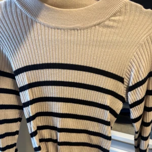Beige och svart randig ribbad tröja - Säljer en snygg beige tröja med svarta ränder. Helt ny aldrig använd. Tröjan är ribbad och har långa ärmar, från lager nypris 150kr. Köparen står för frakten!