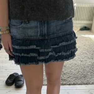 Jeanskjol med volanger - Snygg jeanskjol med flera lager av volanger. Perfekt för en avslappnad stil. Kjolen har en klassisk jeansfärg och är kort i modellen. Den har en resår i midjan så den passar mig med Xs/S