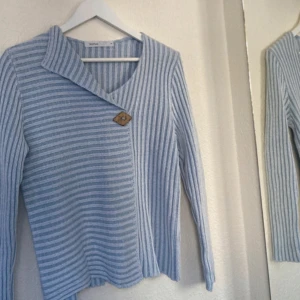 Unik kofta - Snygg grå och vit randig tröja från Skovhuus med en unik omlott-design och en dekorativ knapp. Tröjan har en v-ringad hals och långa ärmar!💙