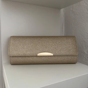 Glittrig kuvertväska från Anna Field - Snygg glittrig kuvertväska från Anna Field i en elegant guldig nyans.🫶 Väskan har en stilren design med en kedja som kan användas som axelrem. Perfekt för t.ex bal eller annan tillställning❣️❣️Ändast använd 1 gång