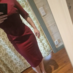 Vinröd retro klänning från Aida Zak - Snygg vinröd klänning från Aida Zak med kort ärm och en elegant passform. Klänningen har en liten öppning med knappar i nacken och en diskret dragkedja i ryggen. Super bekväm tyget har börjat noppa sig lite, tyvärr.