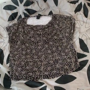 Svart och vit mönstrad topp från Lindex - Säljer en svart och vit mönstrad topp från Lindex. Toppen har en lös passform och korta ärmar, perfekt för en avslappnad stil. Tillverkad i mjukt och bekvämt viskosmaterial.