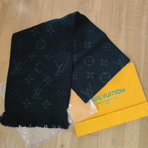 Svart halsduk från Louis Vuitton - Elegant svart halsduk från Louis Vuitton med ikoniskt mönster. Tillverkad i en lyxig blandning av ull och silke, vilket ger en mjuk och varm känsla. Perfekt för att ge en stilfull touch till din outfit. Fransen i ändarna ger en extra detalj.
