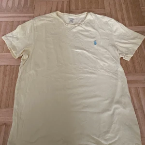 T-shirt från Polo Ralph Lauren - Säljer en t-shirt från Polo Ralph Lauren med en broderad blå logga på bröstet. T-shirten är kortärmad och tillverkad i bomull, perfekt för en avslappnad stil. Obs tröjan är ljusgul men det var svårt att få med i bild