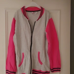 Grå och rosa jacka från Mix - Säljer en cool grå och rosa jacka från Mix. Jackan har långa ärmar och dragkedja framtill. Den har ribbade muddar i rosa och svart vid ärmslut och nederkant, samt praktiska fickor med rosa detaljer. Perfekt för en färgglad stil!