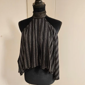 Svart och vit randig halterneck topp - Snygg svart halterneck topp med silver ränder. Toppen har en lös passform och är perfekt för en stilren look. Materialet är mjukt och faller fint.