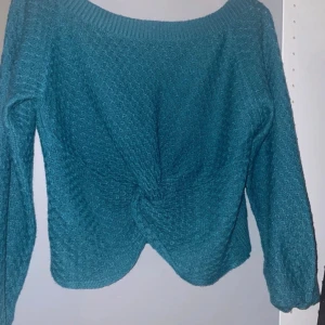 Turkos stickad tröja - Säljer en snygg turkos stickad tröja med en unik twistdetalj framtill. Tröjan har långa ärmar och en rund halsringning. Perfekt för kyligare dagar!