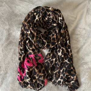 Leopardmönstrad halsduk från Victoria's Secret - Snygg leopardmönstrad halsduk från Victoria's Secret med rosa detaljer. Perfekt för att ge din outfit en djärv touch. Den är lätt och passar bra för olika tillfällen. Helt ny med lapp kvar!
