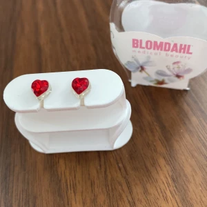 Röda hjärtformade örhängen från Blomdahl - Snygga hjärtformade örhängen från Blomdahl i en intensiv röd färg. Tillverkade i naturligt titan, vilket gör dem perfekta för känsliga öron. Perfekta för att lägga till en färgklick till din outfit!