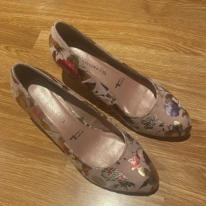 Blommiga pumps från Tamaris - Säljer ett par eleganta pumps från Tamaris med blommigt mönster i flera färger. Skorna har en bekväm klack och en spetsig tå, vilket ger en stilren look. Perfekta för att sätta färg på din outfit! köpt för ca 1600 kr