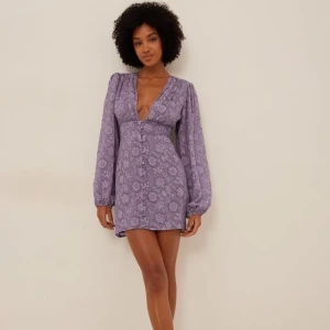 Lila blommig klänning - Säljer en lila blommig klänning med v-ringning och långa ärmar. Klänningen har knappar framtill. Endast testad och säljs då jag köpte fel storlek. 