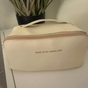 Beige necessär från Rose of No Man's Land - Snygg beige necessär med dragkedja och praktiskt handtag. Perfekt för att organisera dina småsaker. Stilren design med guldiga detaljer.