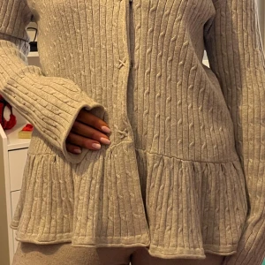 Beige ribbad kofta - Säljer en beige ribbad kofta med volangdetalj vid nederkanten. Koftan har långa ärmar och knäppning framtill. Perfekt för en mysig och stilren look. jag har strl S som referens!