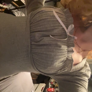 Grå ribbad topp med knytband - Säljer en stilren grå ribbad topp med långa ärmar och ett sött knytband framtill. Perfekt för en avslappnad look.