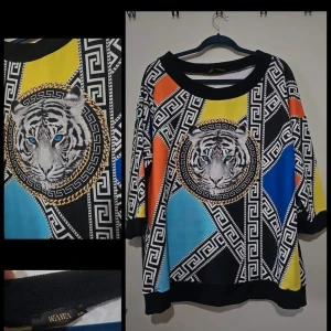 Färgglad tröja med tigertryck från Wawa - Säljer en unik och färgglad tröja från Wawa med ett stort tigertryck i mitten. Tröjan har ett geometriskt mönster i svart, vit, gul, blå och orange. rund halsringning. Perfekt för dig som vill sticka ut!