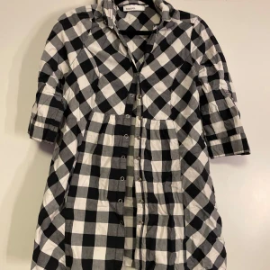 Svartvit rutig klänning från KappAhl - Snygg svartvit rutig klänning från KappAhl med trekvartsärm och knappar framtill. Perfekt för en avslappnad stil med en klassisk touch. Den har en bekväm passform och är lätt att matcha med olika accessoarer. Storlek 38!