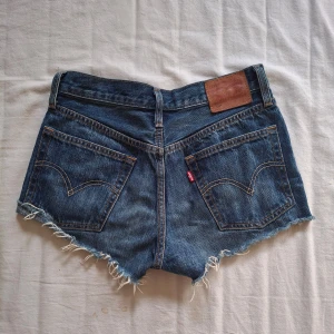 Blå jeansshorts med fransar - Snygga blå jeansshorts från Levi's med fransiga kanter och klassisk femficksdesign. De har en knappgylf och en läderpatch baktill och är köpta i Budapest. Använda sparsamt (: