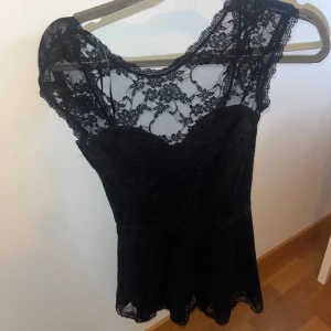 Svart spetstopp - Elegant svart topp med vacker spetsdetaljering. Den har en figurnära passform och är perfekt för festliga tillfällen. Klänningen är ärmlös och har en fin, feminin design.