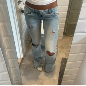 Ljusblå bootcut jeans med slitningar - Snygga ljusblå bootcut jeans med slitningar på knäna. De har en låg midja och en klassisk femficksdesign. Innerbenslängd 80cm, midja rakt över ca 40💕 Sydda lågmidjade själv kom privat för bilder på de, och de har ett hål vid ena hälen