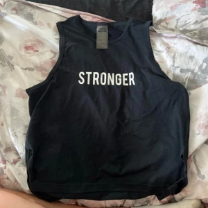 Svart linnetopp från Stronger - Snygg svart linnetopp från Stronger med texten 'STRONGER' i vitt på framsidan. Perfekt för träning eller en avslappnad dag. Tillverkad i mjukt material för extra komfort.