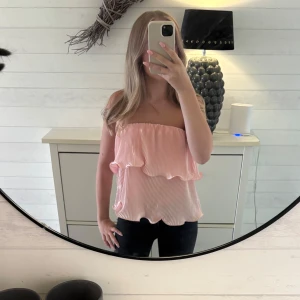 Ljusrosa bandeau tubtopp med volanger - Supersöt ljusrosa bandeau tubtopp med dubbla volanger och plisserad struktur. Toppen är axelbandslös och har en flowy, luftig känsla som passar perfekt till sommaren. Använd nån gång bara. 