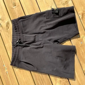Svarta shorts från Stone Island - Svarta shorts från Stone Island med klassisk logga på benet. Mjukt bomullsmaterial, elastisk midja med snörning och praktiska fickor. Perfekta för chill dagar eller när du vill ha en clean streetwear-look.
