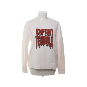 Vit sweatshirt från Maje med tryck - Cool vit sweatshirt från Maje med stort rött och svart tryck 'Enfant Terrible' på bröstet. Tröjan har rund hals, långa ärmar och är gjord i mjuk bomull. Perfekt för dig som gillar statement-plagg och streetstyle. Har en fläck på ärmen som syns på bild 2, om man kollar lite extra noggrant!