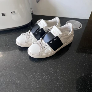 Valentino Garavani vita sneakers - Tjena, Säljer ett par snygga Valentino Garavani sneakers i vitt skinn med bred svart rem över foten och coola nitar på hälen strlk 41 passar 42. Köpta på NK i Stockholm 5999kr, tyvärr medföljer ingen låda då den hivats pga flyttning, skick 7,5/10!! ”priset går självklart att diskuteras” Tveka inte på att höra av dig vid eventuella frågor  eller funderingar🤝🏻