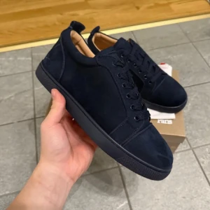 Mörkblåa Skor  från Christian Louboutin - HELT NYA SKICK 10/10 Snygga matinblåa sneakers från Christian Louboutin med klassisk rund tå och ikonisk röd sula. Skorna har svart snörning, diskret logga och är tillverkade i ett slätt material med beige innersida. Perfekta för dig som vill sticka ut med stilrena detaljer.