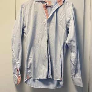 Ljusblå skjorta från Stenströms - Snygg ljusblå skjorta från Stenströms med slimline-passform. Skjortan har coola detaljer i röd- och vitrandigt tyg på insidan av krage och manschetter, samt vita och röda knappar. Tillverkad i mjuk och exklusiv bomull. Perfekt för dig som gillar stilrena plagg med twist.