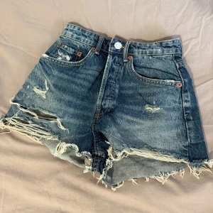 Blå slitna jeansshorts från Zara - Snygga blå jeansshorts från Zara. Shortsen har slitna detaljer och klassisk femficksdesign. Perfekta för en avslappnad och trendig look under sommaren.