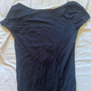 Svart topp med djup rygg från Gina Tricot - En svart, tight topp från Gina Tricot i mjuk bomull. Toppen har korta ärmar och en riktigt djup, rundad rygg som ger en snygg och stilren look. Perfekt att styla med jeans eller kjol för en trendig vibe.