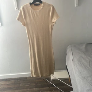 Beige ribbad klänning från Sister - Säljer en beige ribbad klänning från Sister i storlek S. Klänningen har korta ärmar, rund halsringning och är figurnära med en enkel, stilren design. Perfekt för dig som gillar minimalistisk och clean look. Materialet är mjukt och stretchigt för skön passform.