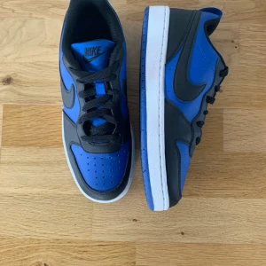 Nike Dunk Low blå sneakers - Snygga Nike Dunk Low sneakers i blått och svart med vit mellansula och blå yttersula. Skorna har klassisk snörning, rund tå och är tillverkade i syntet och skinn. Använd väldigt få gånger så väldigt fint skick! Skriv om ni vill ha fler bilder så fixar jag🤗