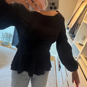 Svart blus med knyt i midjan - Säljer en svart blus med långa ärmar och snyggt knyt i midjan som ger en markerad siluett.